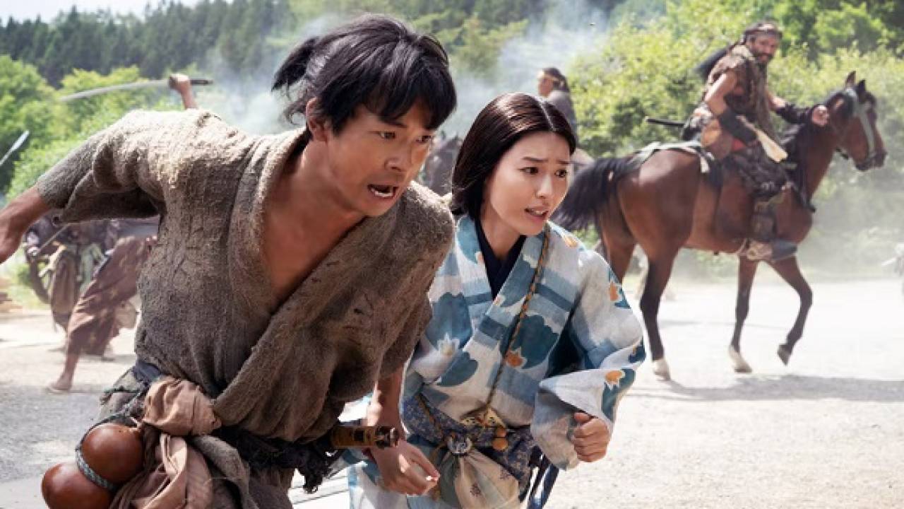 豊臣兄弟!の劇中シーン。秀長役の仲野太賀と女性キャストが馬に乗った武者の前で逃げるように走っている